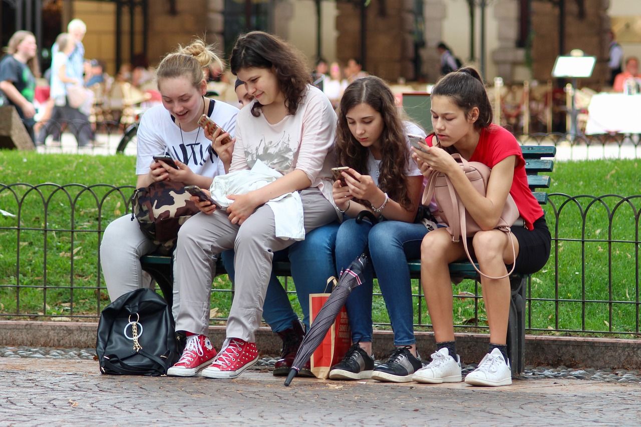 Teenage girls sitting next to adult women and using their phones